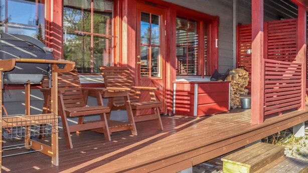 A wooden deck with a table and chairs, a hanging light fixture, and a stack of firewood. - Villa hytönen 1 by Interhome (Äkäslompolo)