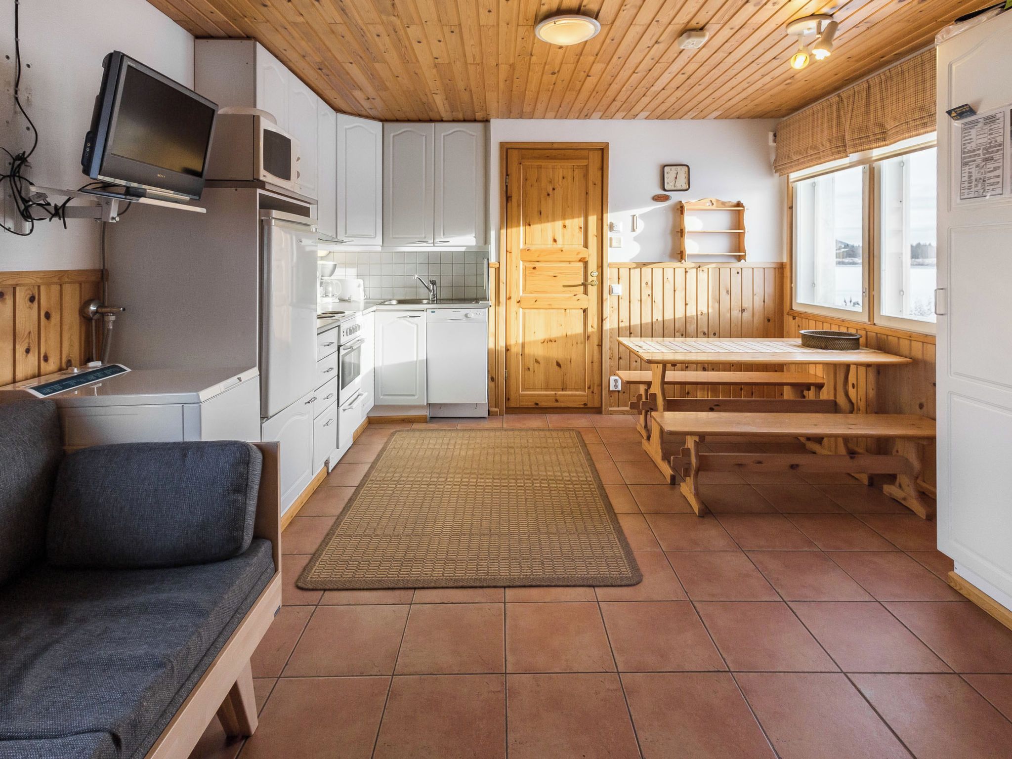 Cocina compacta con armarios blancos, puerta de madera, una mesa de comedor y un banco.