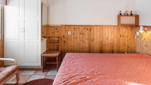 A bedroom with a wooden headboard, a bed with a pink quilt, a wooden chair, a white wardrobe, and a shelf with decorative items. - Tammukka i by Interhome (Äkäslompolo)