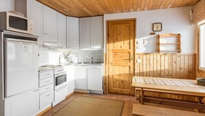 A compact kitchen with white cabinets, a microwave, an oven, and a dishwasher. There's a wooden door, a small table, and a bench. - Tammukka i by Interhome (Äkäslompolo)