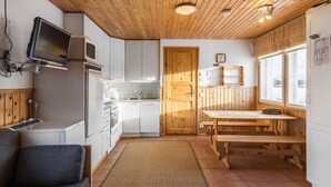 A compact kitchen with white cabinets, a wooden ceiling, and a dining area with a bench. - Tammukka i by Interhome (Äkäslompolo)
