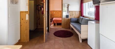 A compact room with a bed, a sofa, a kitchenette, and a door leading to another room.