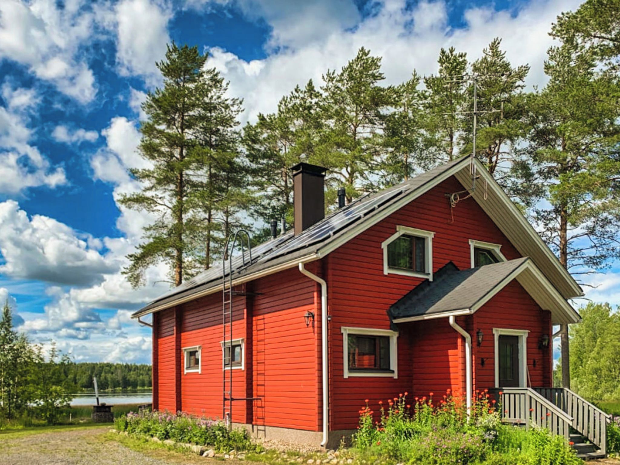 Punainen puutalo, jossa on savupiippu, ikkunat ja kuisti.