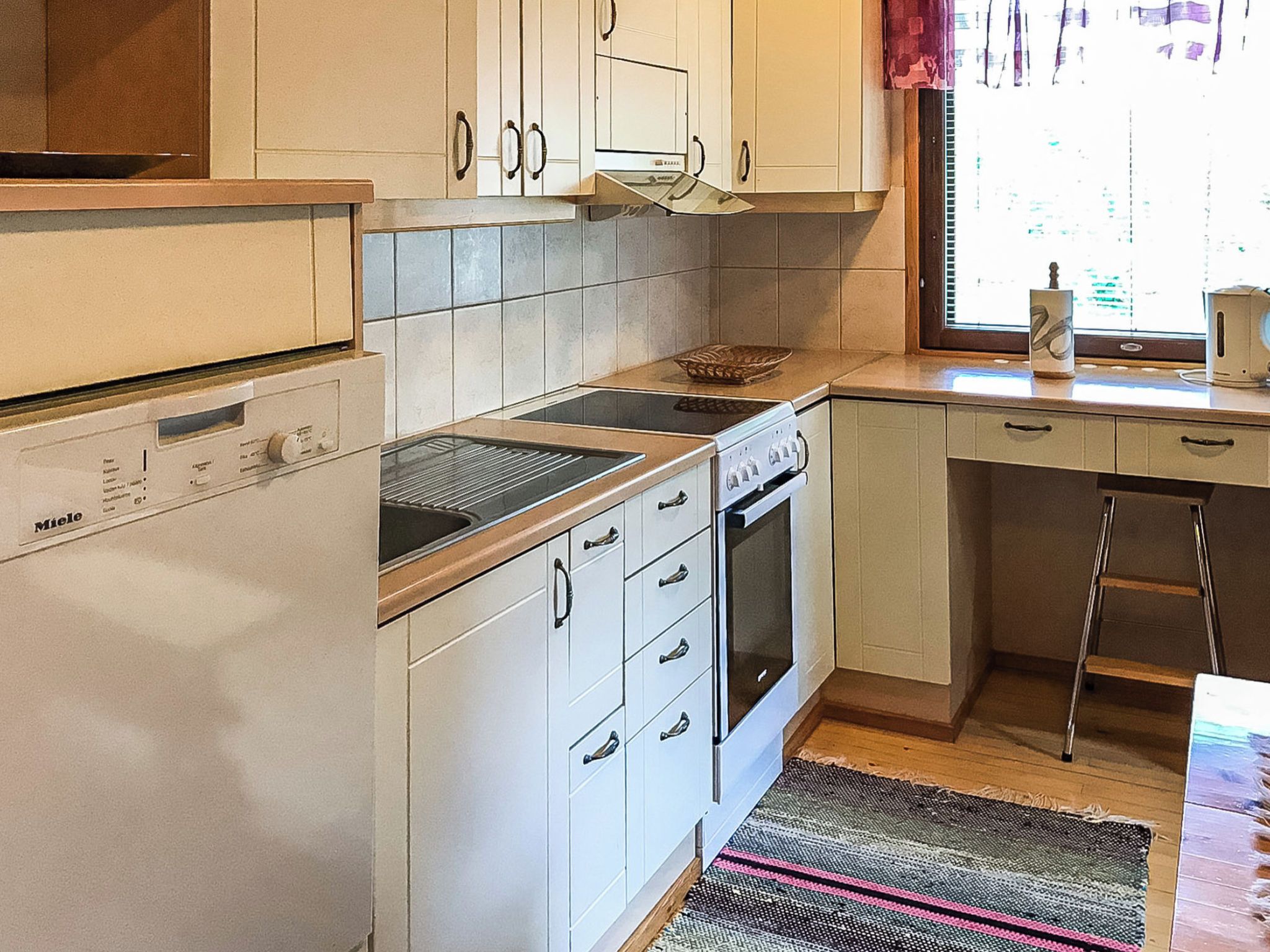 Een kleine keuken met witte kastjes, een inbouwmagnetron, een fornuis en een oven.