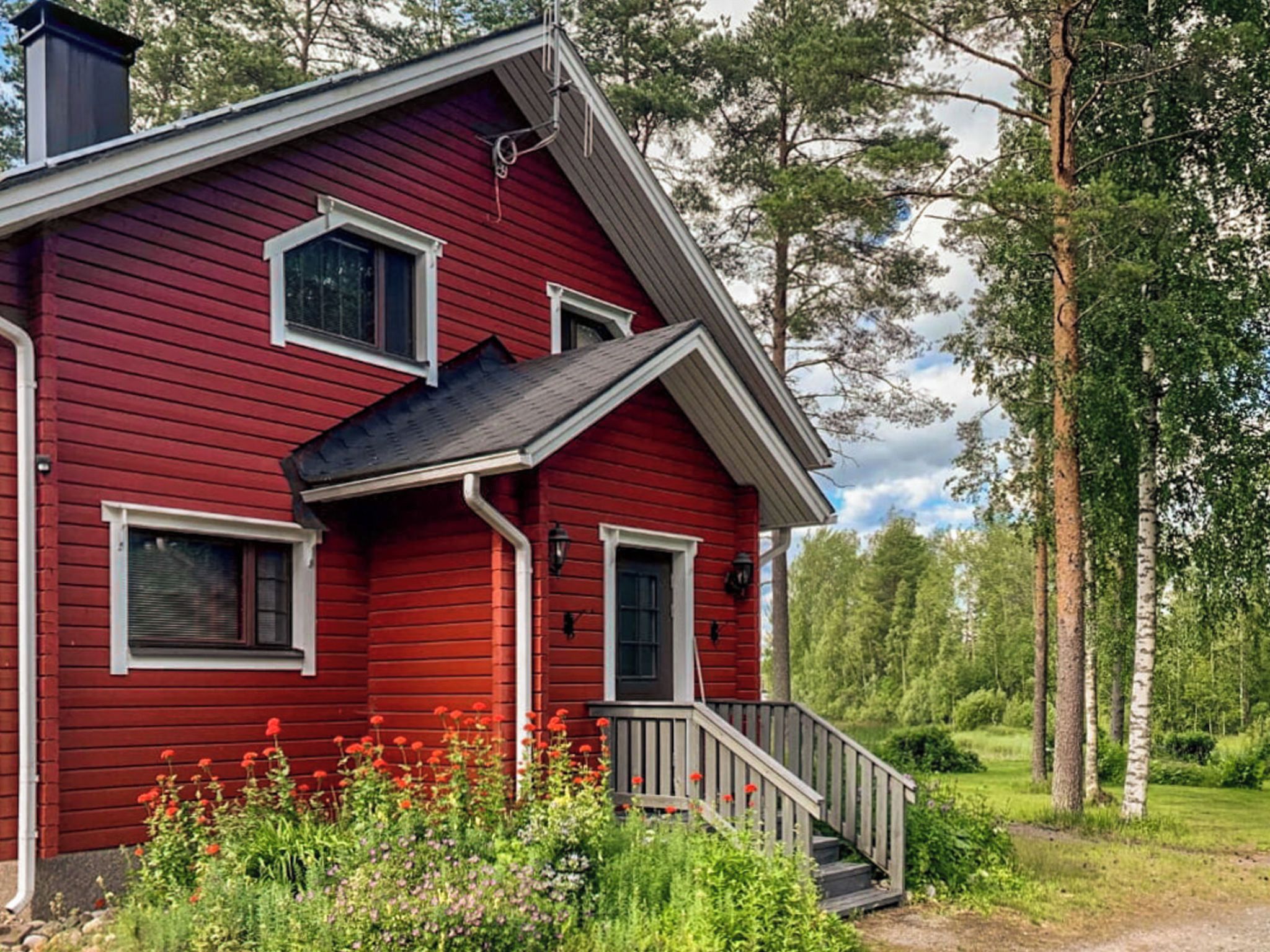 A red wooden house with a porch, windows, and a chimney.