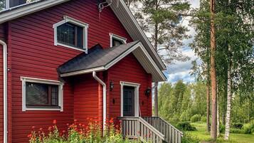 A red wooden house with a porch, windows, and a chimney.