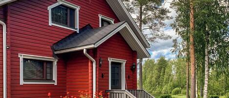 A red wooden house with a porch, windows, and a chimney.
