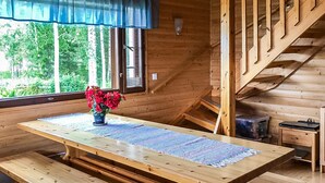 A wooden cabin interior with a dining table, benches, a staircase, and a window with a view of trees. - Kallioniemi by Interhome (Kiuruvesi)