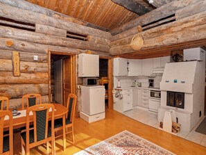 A log cabin interior with a dining area, kitchen, and a fireplace.