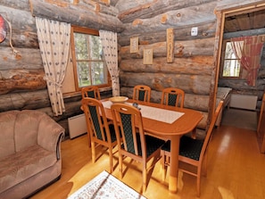 A cozy log cabin interior with a dining table, four chairs, a sofa, and a window with curtains. - Rukanlumous 1 by Interhome (Kuusamo)