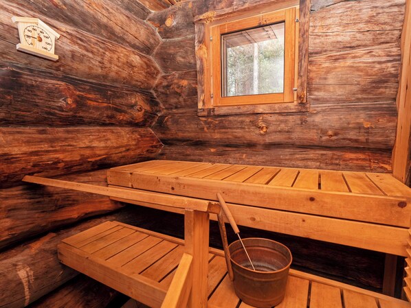 A rustic wooden cabin interior with a wooden bench, a window, and a wooden bucket.