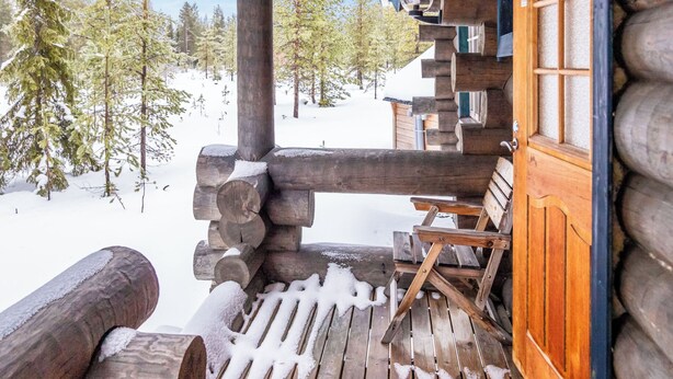 Uma cabana de madeira com um deck coberto de neve e paredes de tronco.