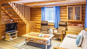 Interior de uma cabana de tronco com escada de madeira, televisão, sofá e um armário com portas de vidro.