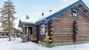 Uma cabana de tronco com telhado íngreme e fachada coberta de neve.
