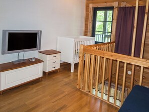 A room with a wooden floor, a white dresser, a television, a white radiator, and a window with a view of greenery. - Kultakoto b by Interhome (Nilsiä)