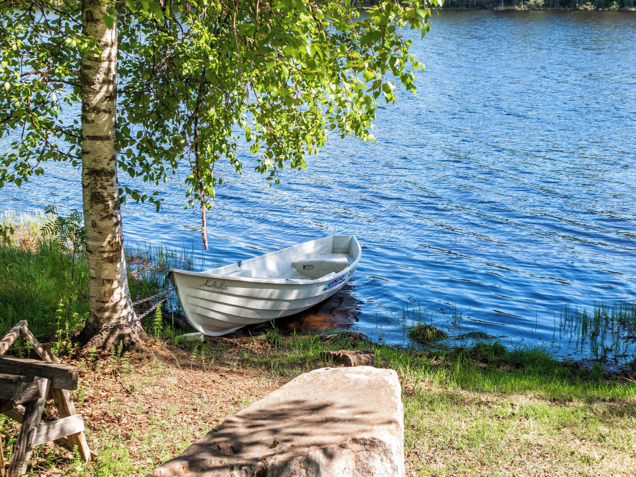 Ein Boot mit dem Namen 'Kultakolo' liegt an einem Baum an einem ruhigen See.