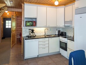 A compact kitchen with white cabinets, a built-in microwave, a coffee maker, and a stove. - Kultakoto b by Interhome (Nilsiä)