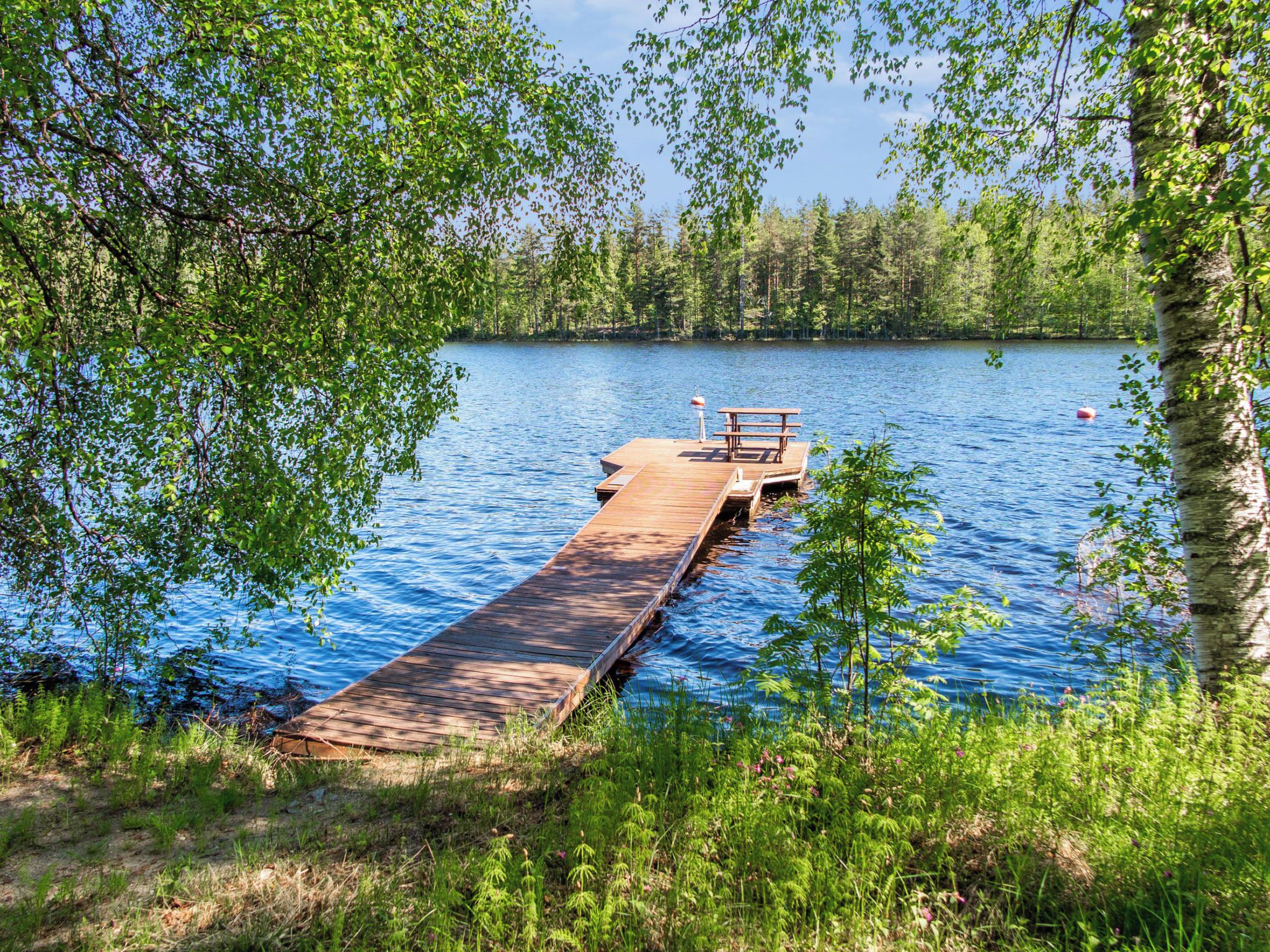 A wooden dock extending into a calm lake surrounded by dense trees.