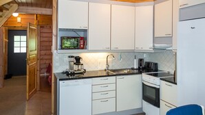 Eine kleine Küche mit weißen Schränken, einer Mikrowelle, einer Kaffeemaschine, einem Spülbecken und einem Herd.