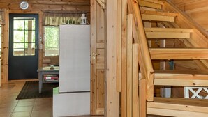 Ein Interieur einer Holzhütte mit Treppe, Kühlschrank, Fenster und Tür.