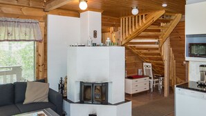 Ein gemütliches Blockhaus-Interieur mit Kamin, Holzbalken, einer Couch, einem Essbereich und einer Küche.