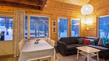 Indretning i en hyggelig hytte med spisebord, sofa og stort vindue med udsigt over et sneklædt landskab.