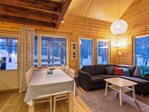 A cozy cabin interior with a dining table, sofa, and a large window with a view of a snowy landscape. - Kevätpiippo b by Interhome (Ylläsjärvi)