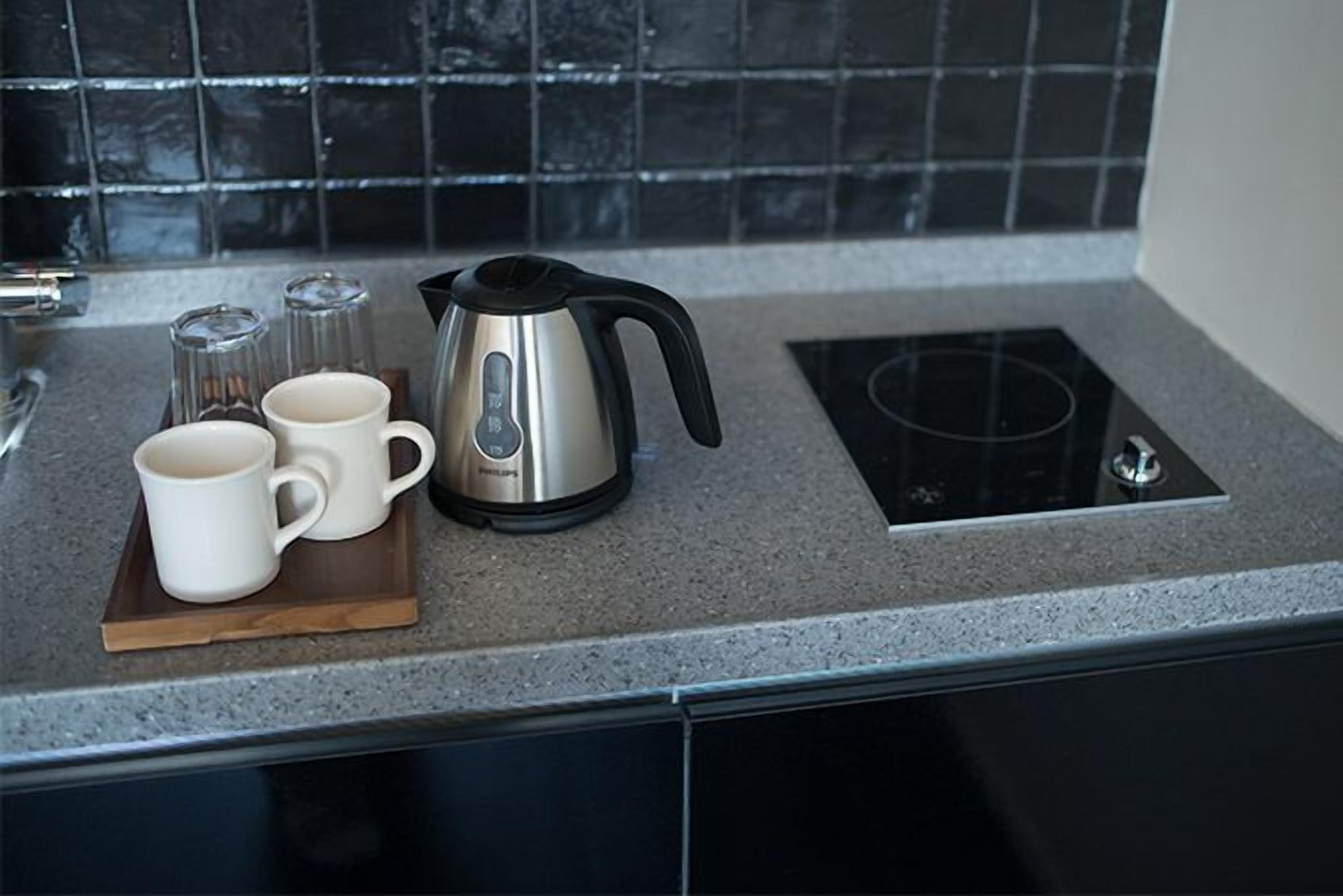 A kitchen counter with a kettle, two white mugs, and salt and pepper shakers.