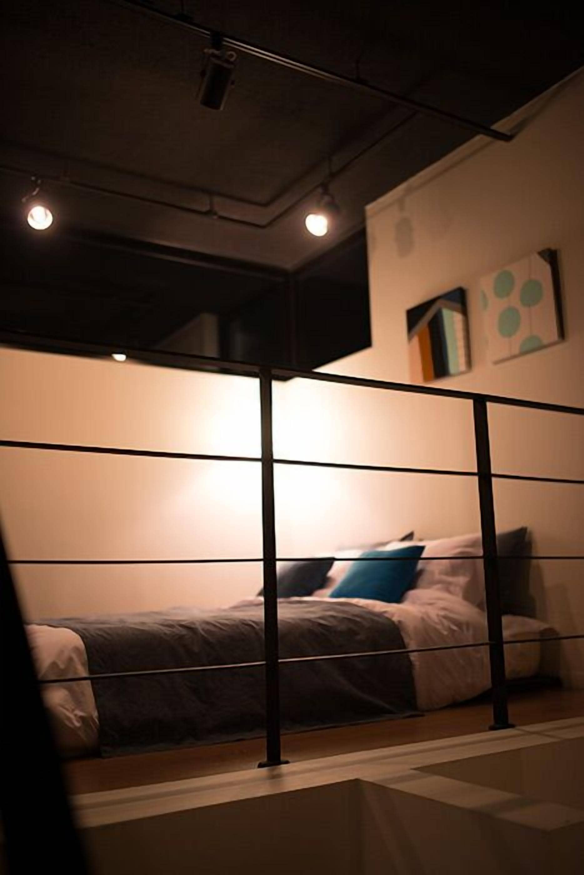 A dimly lit room with a bed, a metal railing, and a wall with abstract art.