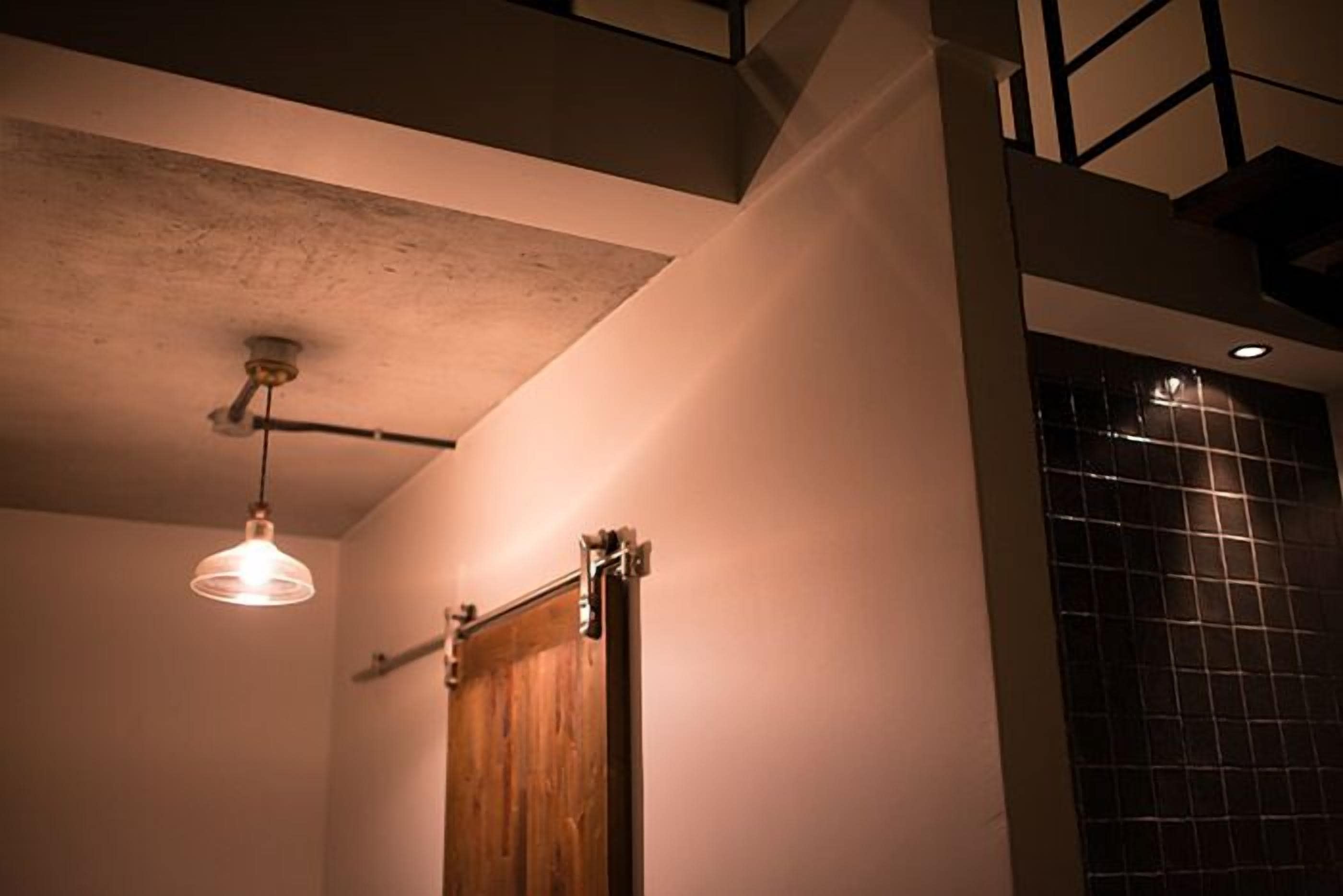 Une pièce avec une porte en bois, un luminaire suspendu et un mur recouvert de carreaux.