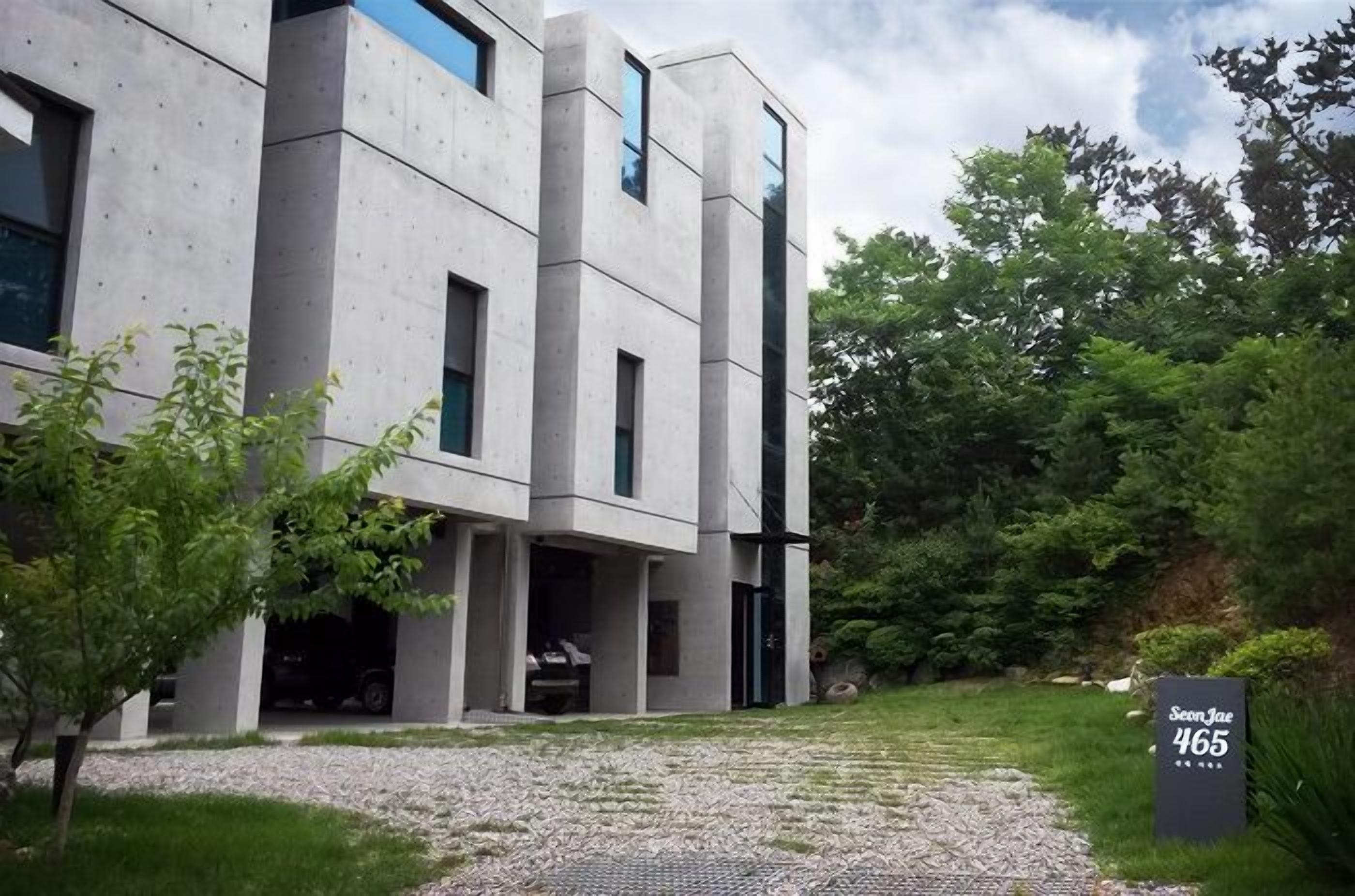 A modern building with a concrete facade, multiple windows, and a gravel driveway.