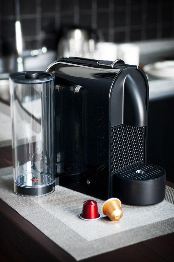 Une cuisine équipée d’une machine à café, d’un récipient en verre et de deux dosettes de café posées sur un plan de travail.