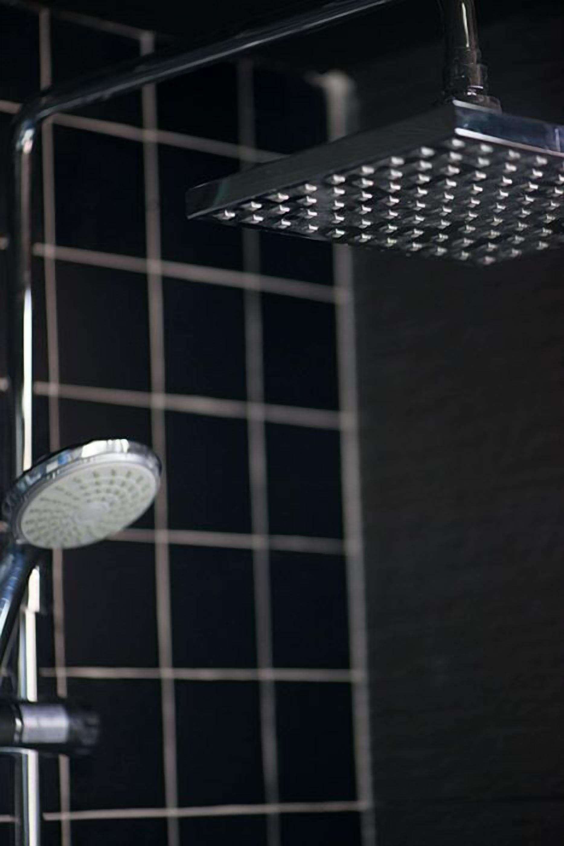 Une douche moderne dotée d’un pommeau de douche à effet pluie et d’un flexible de douche.