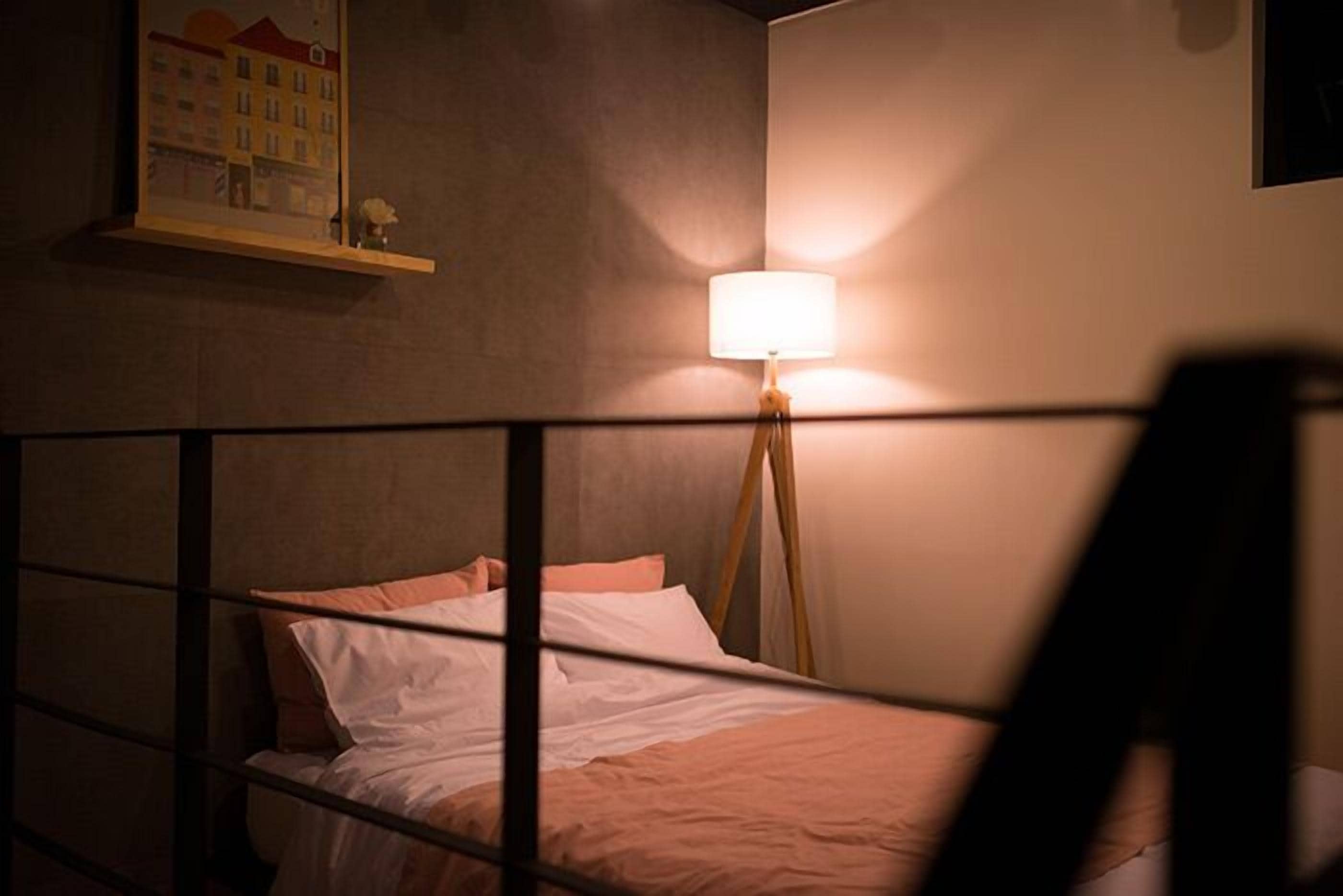 A bedroom with a bed, a bedside lamp, and a wall-mounted shelf with a framed picture.