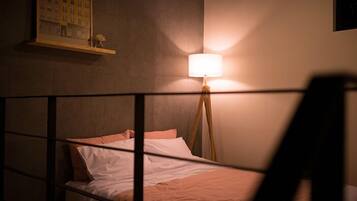 A bedroom with a bed, a bedside lamp, and a wall-mounted shelf with a framed picture.