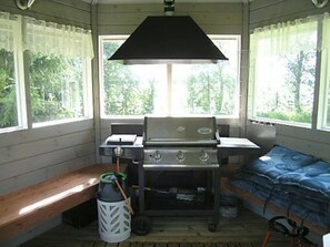 A cabin interior with a wooden bench, a stove, and a window with curtains.
