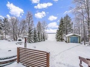 Paisaje nevado con un banco de madera, un cobertizo pequeño y árboles cargados de nieve.