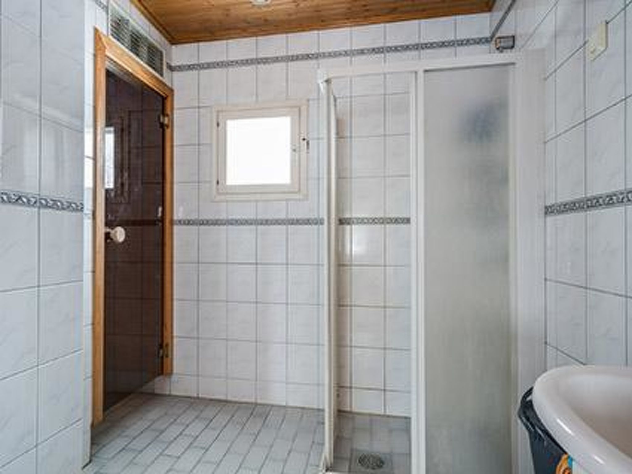 Un baño con paredes de azulejos blancos, techo de madera, cabina de ducha y bañera.