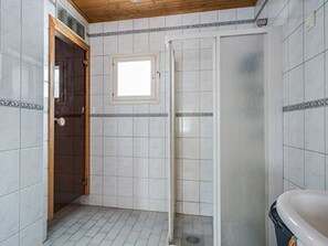 Un baño con paredes de azulejos blancos, techo de madera, cabina de ducha y bañera.