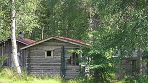 Eine rustikale Holzhütte mit rotem Dach, umgeben von üppigem Grün.