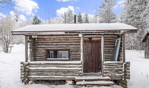 A rustic log cabin with a wooden door and window, surrounded by snow.