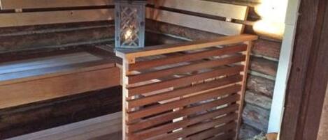 Uma sauna de madeira com parede de pedra e um recipiente de metal com a etiqueta 'NATURAL'.