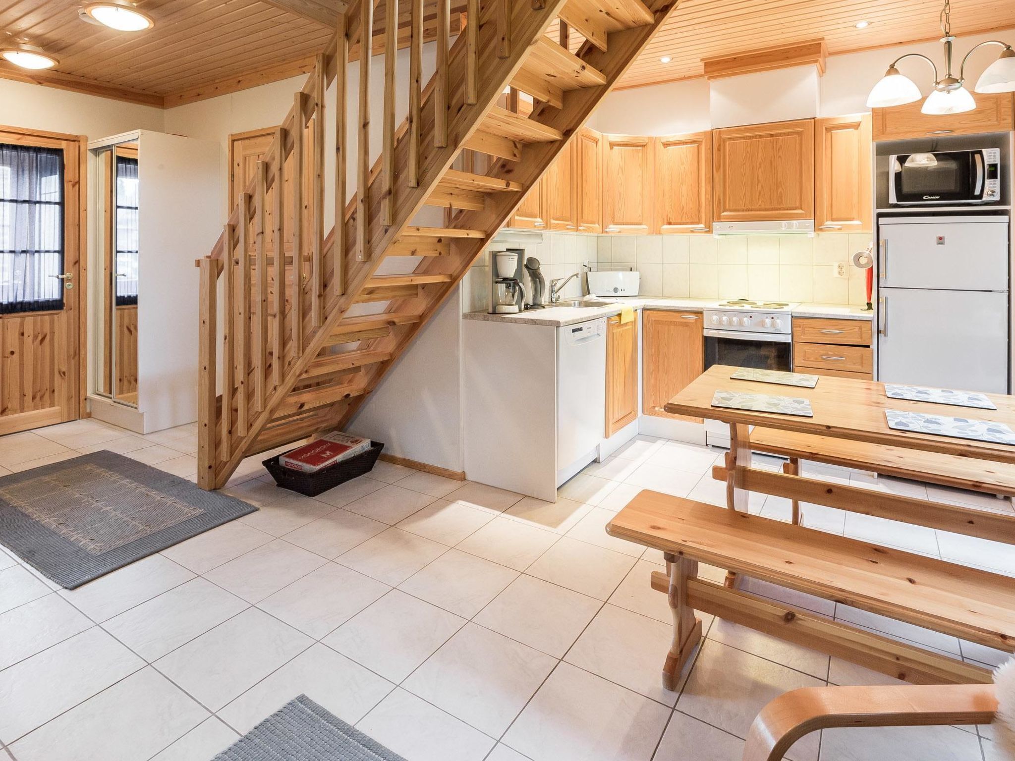 A kitchen with wooden cabinets, a wooden staircase, a dining table, and a refrigerator.