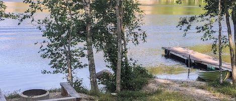 Un paisaje junto al lago con un muelle, un banco y un bote.