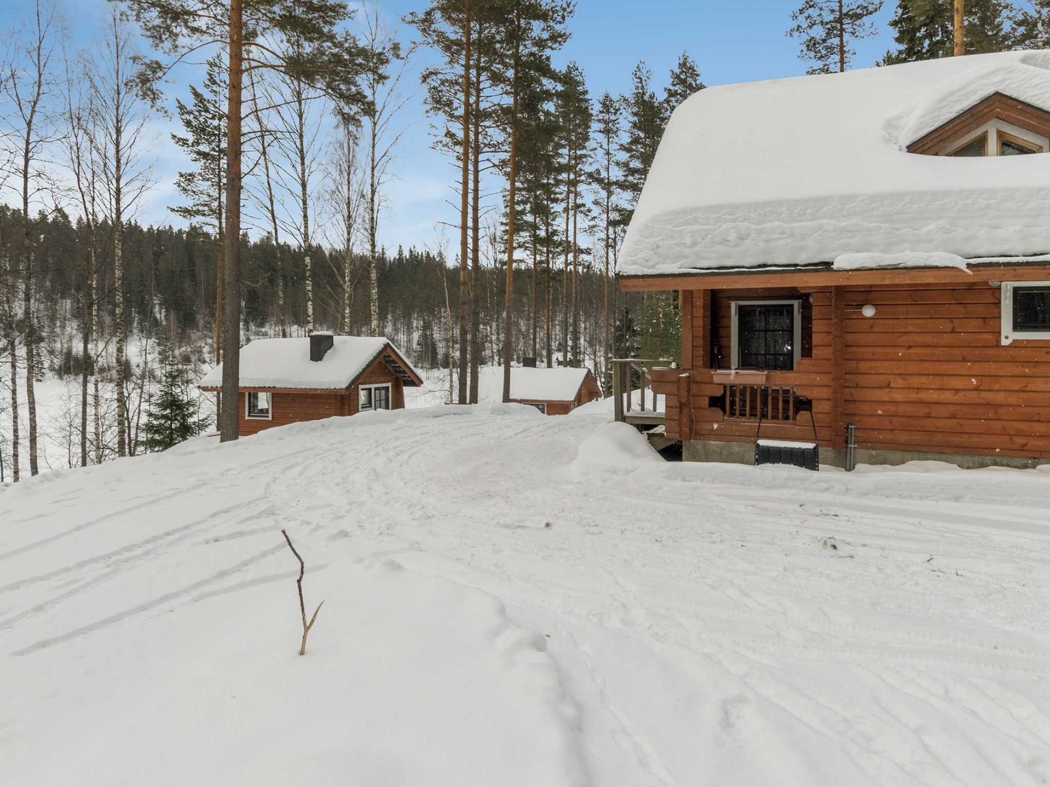 A cabin with a wooden exterior and a snow-covered roof, surrounded by a forest.