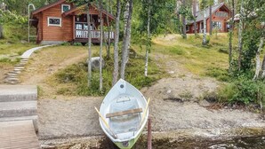 Une cabane en bois avec un porche, un bateau amarré au bord de l’eau et un sentier menant à la cabane.