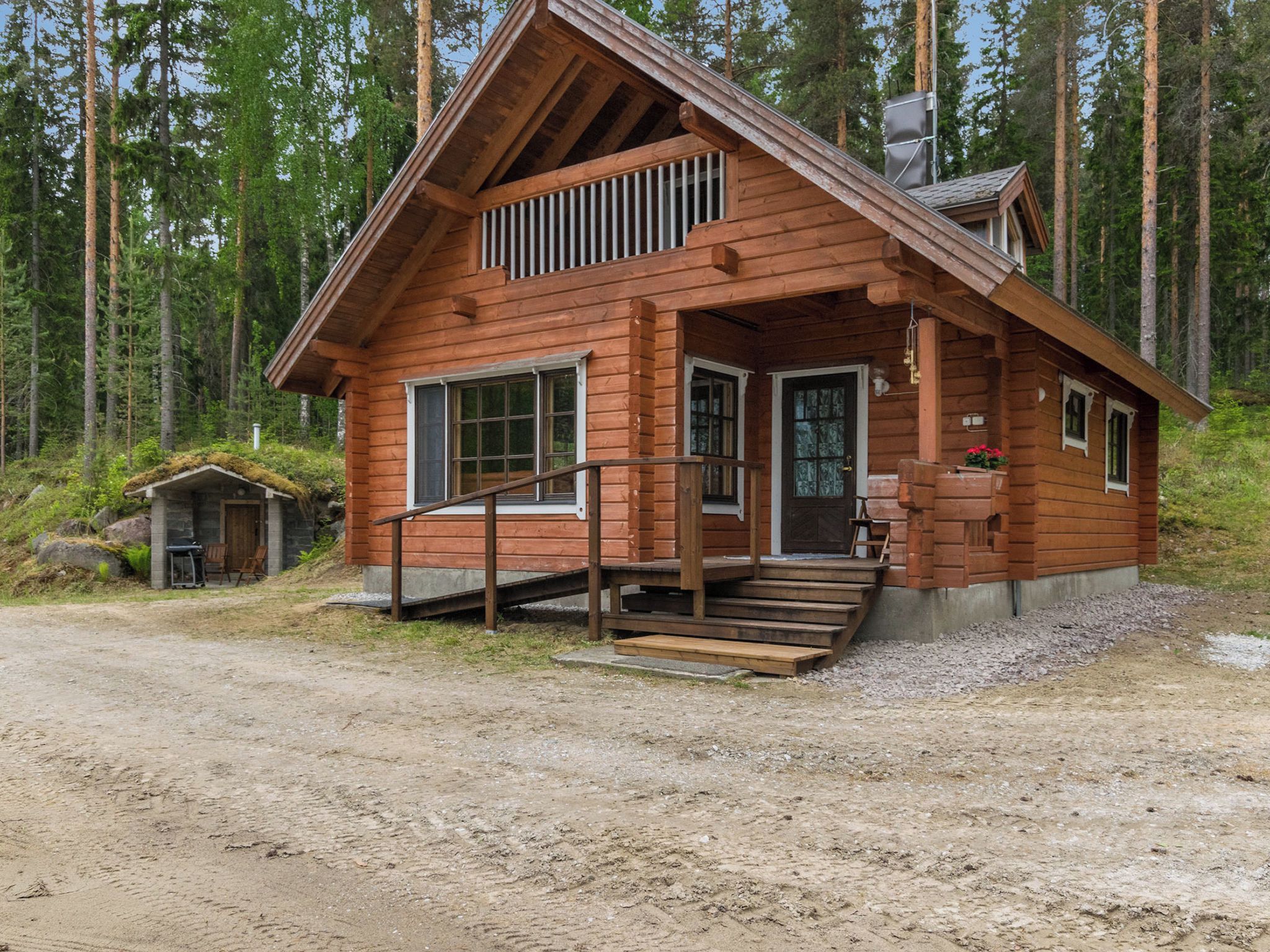 Une cabane en bois avec une véranda, une petite dépendance attenante et un chemin de terre menant à l’entrée.
