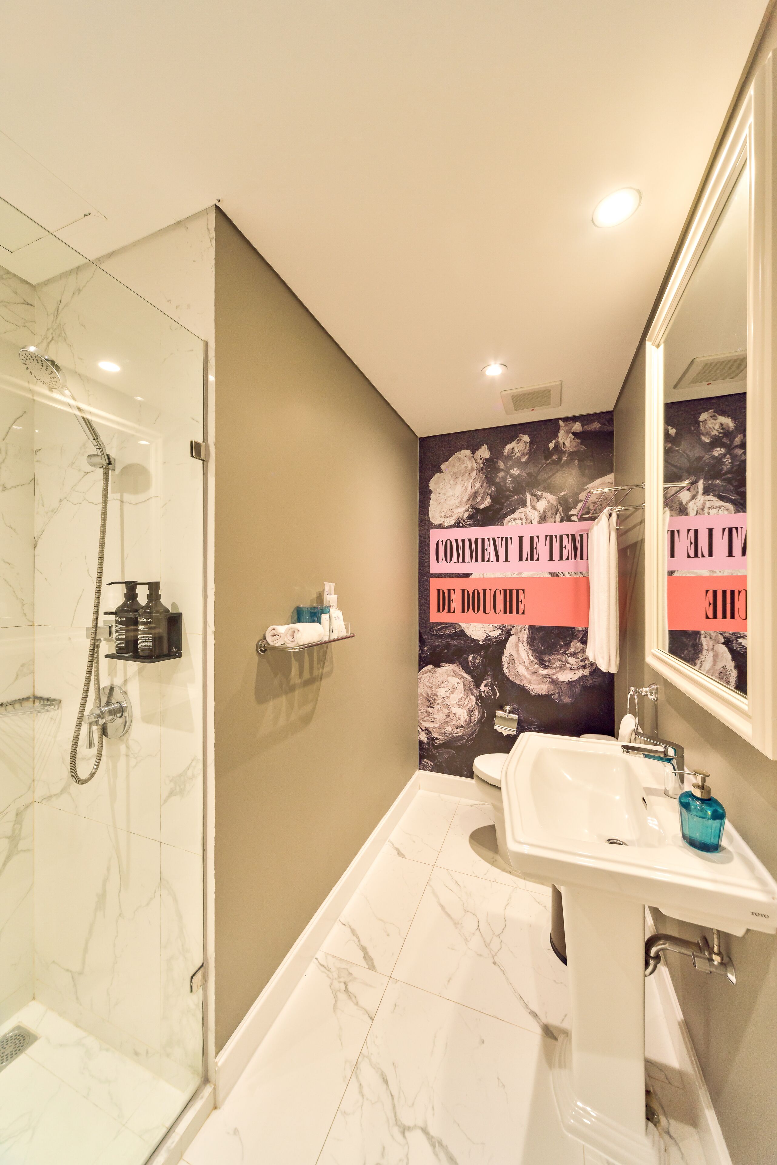 A modern bathroom with a glass-enclosed shower, a white sink, and a large mirror.