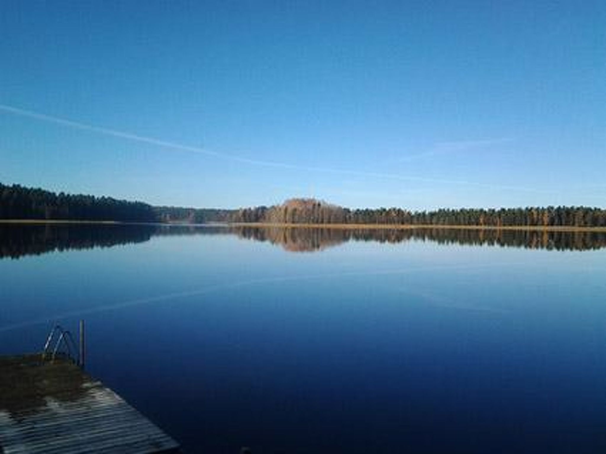 A calm lake with a dock and a forested shoreline.