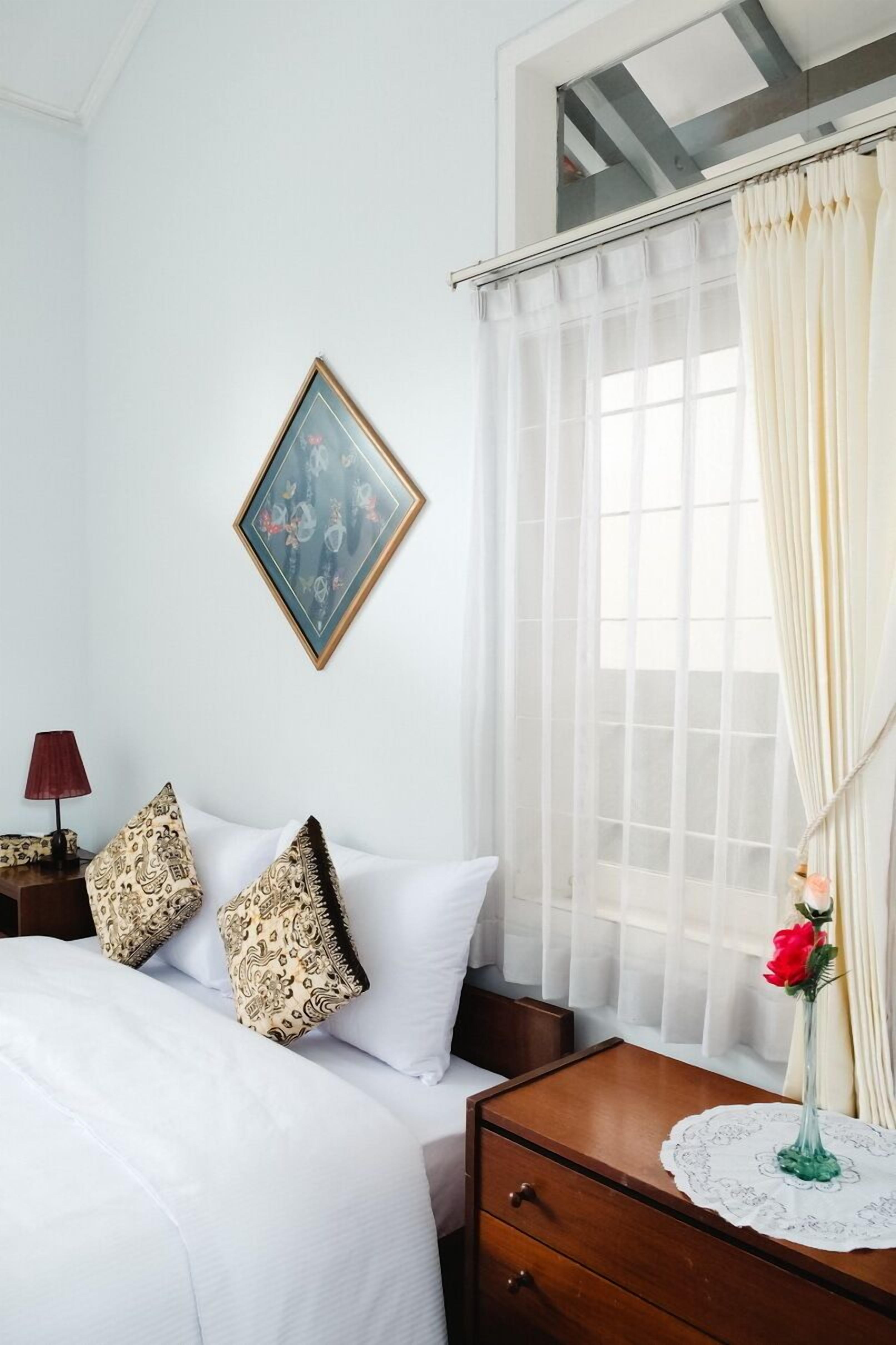 A hotel room with a bed, a nightstand, a lamp, a framed picture, and a window with curtains.